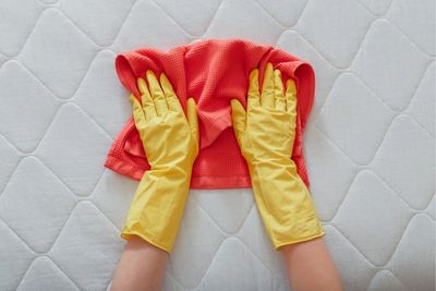 Manos con guantes limpiando un colchón
